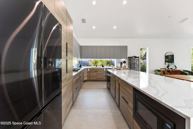 kitchen with modern cabinets, freestanding refrigerator, black microwave, recessed lighting, and light stone countertops
