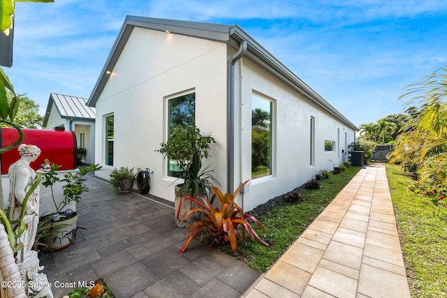 view of home's exterior featuring a patio area, central AC, a standing seam roof, and stucco siding