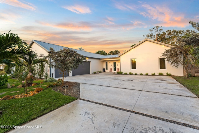 ranch-style house with stucco siding, driveway, a front yard, a garage, and metal roof