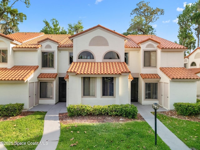 mediterranean / spanish house with stucco siding, a front lawn, and a tile roof
