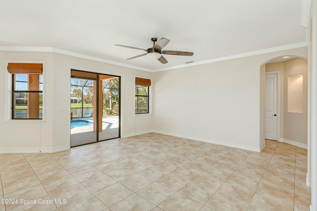 spare room featuring ceiling fan, arched walkways, ornamental molding, light tile patterned flooring, and baseboards