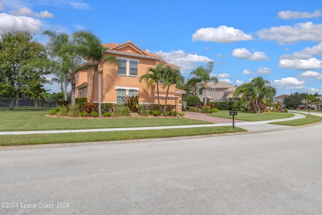 mediterranean / spanish-style home with a tile roof, fence, stucco siding, a front lawn, and driveway