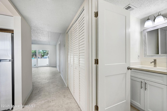 hallway with baseboards, a textured ceiling, a sink, and visible vents