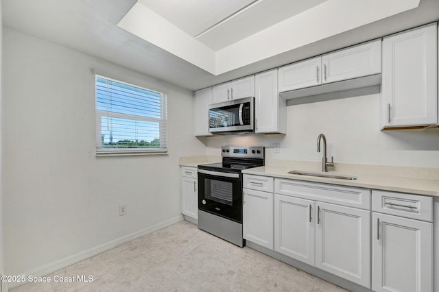 kitchen with light countertops, appliances with stainless steel finishes, a sink, and white cabinetry