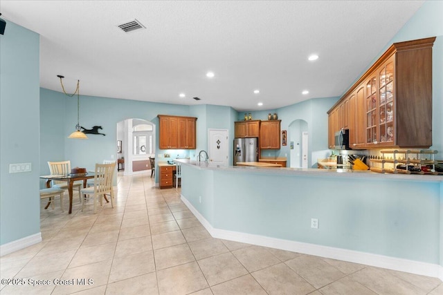 kitchen with glass insert cabinets, arched walkways, visible vents, stainless steel appliances, and brown cabinets
