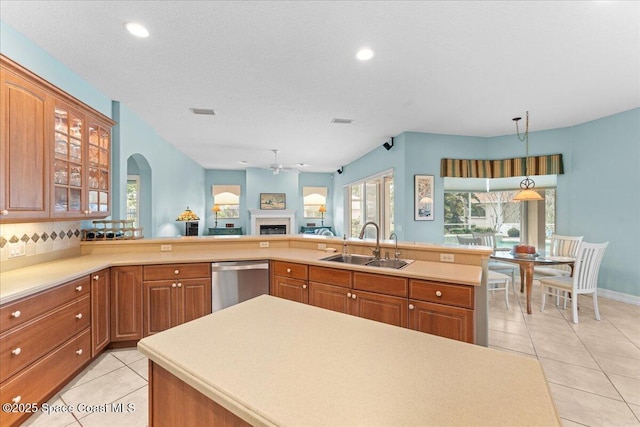 kitchen featuring light tile patterned floors, dishwasher, a sink, a ceiling fan, and brown cabinetry