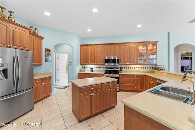 kitchen with tasteful backsplash, light countertops, appliances with stainless steel finishes, arched walkways, and a sink