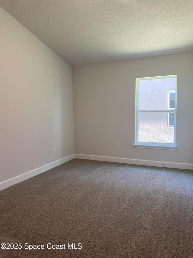empty room featuring dark carpet, baseboards, and a textured ceiling