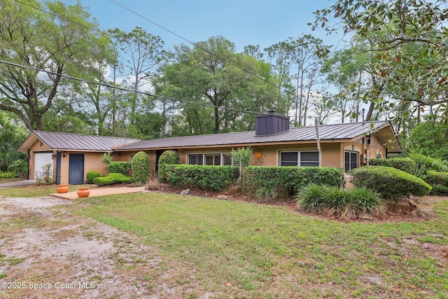 ranch-style home with stucco siding, a chimney, driveway, an attached garage, and metal roof