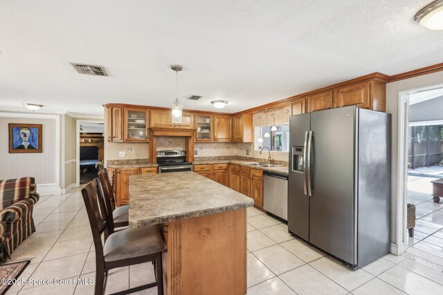 kitchen featuring brown cabinetry, visible vents, appliances with stainless steel finishes, light tile patterned flooring, and a sink