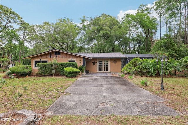 ranch-style house featuring concrete driveway, stucco siding, french doors, a standing seam roof, and metal roof