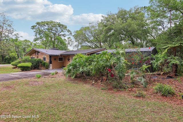 ranch-style house featuring a standing seam roof, a carport, metal roof, a front lawn, and driveway