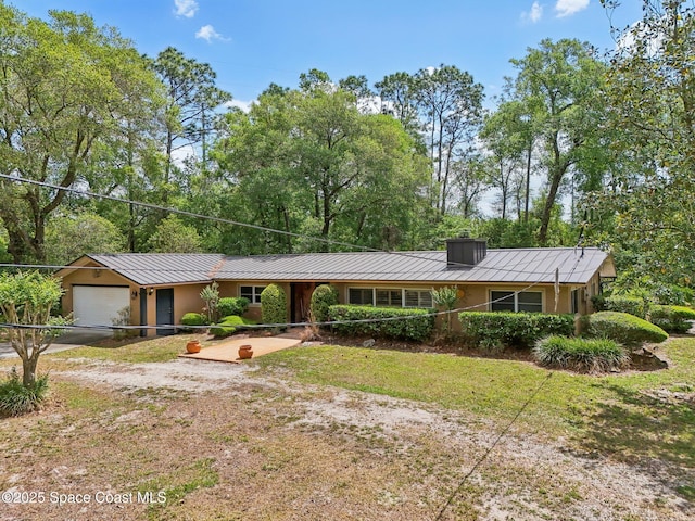 ranch-style home with an attached garage, metal roof, stucco siding, and driveway
