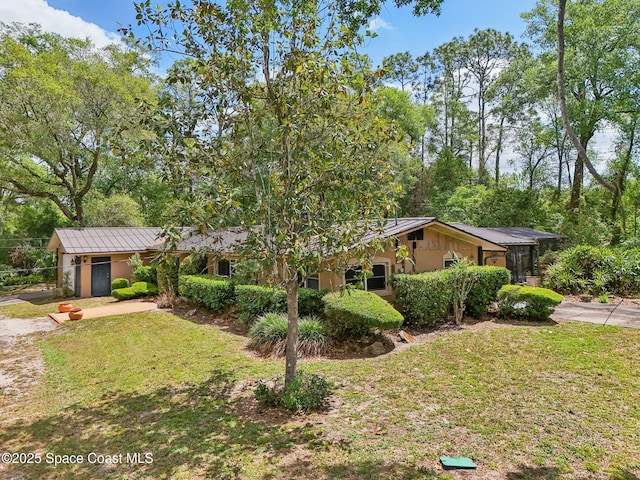 ranch-style home featuring a front yard, a standing seam roof, and stucco siding