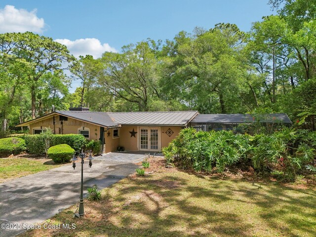 ranch-style house featuring driveway, metal roof, french doors, a front lawn, and a standing seam roof