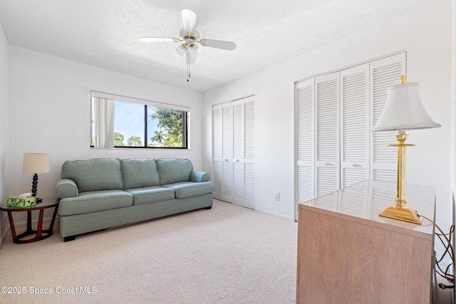 living room featuring baseboards, ceiling fan, a textured ceiling, and light colored carpet