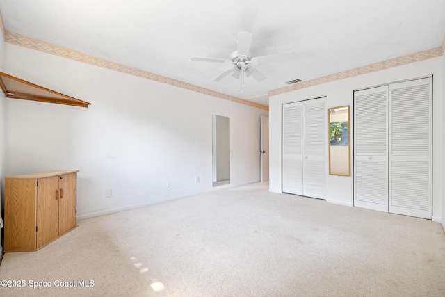 unfurnished bedroom featuring visible vents, multiple closets, light carpet, baseboards, and ceiling fan