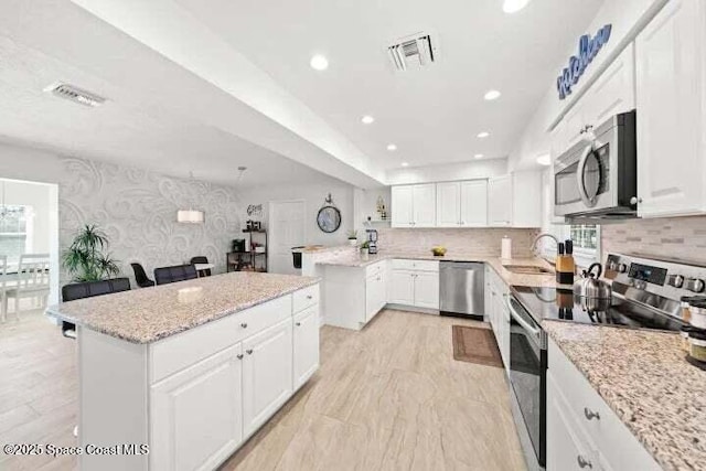 kitchen featuring visible vents, a sink, appliances with stainless steel finishes, light wood-style floors, and wallpapered walls