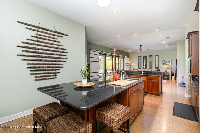 897 Yellow Wood Ct SE, Palm Bay, FL 32909 - kitchen with a ceiling fan, a center island with sink, brown cabinetry, a breakfast bar area, and light wood finished floors