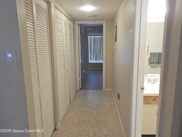 hallway featuring light tile patterned flooring, a sink, a textured ceiling, baseboards, and visible vents