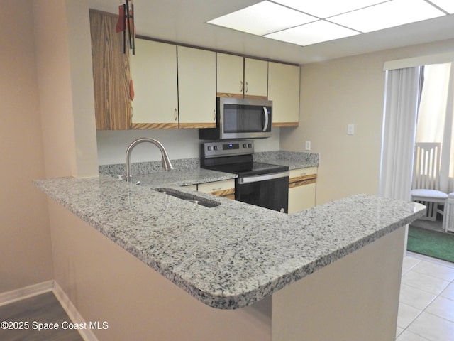 kitchen with light stone countertops, a sink, light tile patterned floors, a peninsula, and stainless steel appliances