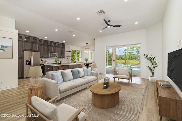 living area featuring light wood-style floors, recessed lighting, a ceiling fan, baseboards, and a high ceiling