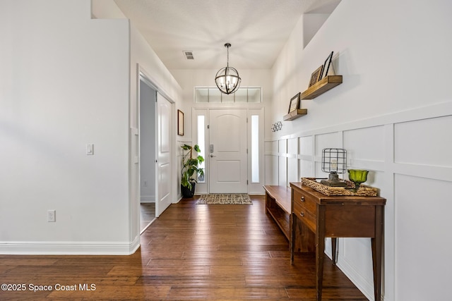 entrance foyer with a decorative wall, hardwood / wood-style floors, visible vents, and an inviting chandelier