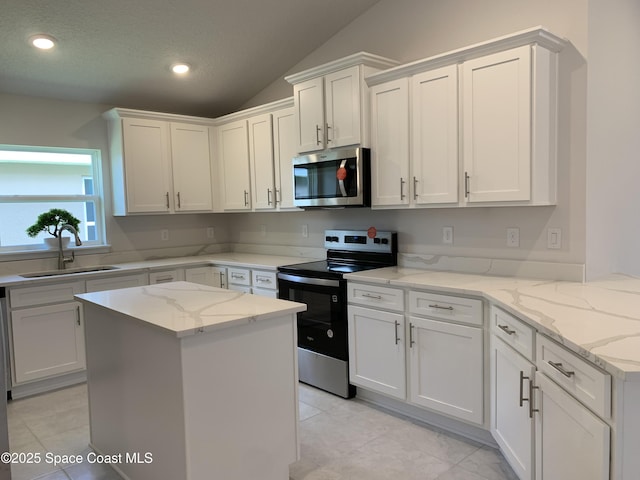 kitchen with light tile patterned flooring, white cabinets, a sink, vaulted ceiling, and stainless steel appliances
