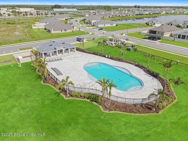 community pool featuring fence, a water view, a lawn, and a residential view