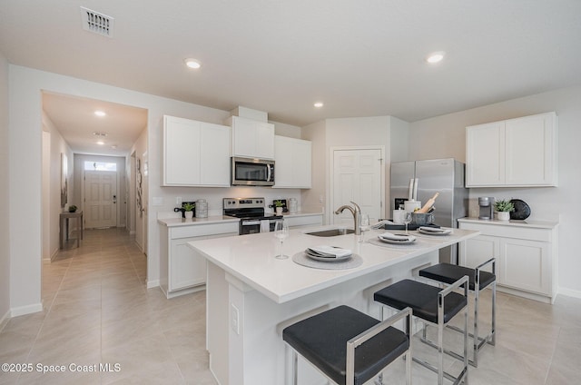 kitchen featuring visible vents, a breakfast bar, appliances with stainless steel finishes, a sink, and a center island with sink