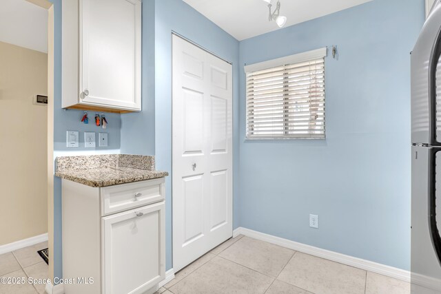 3150 N Harbor City Blvd Unit 236, Melbourne, FL 32935 - kitchen featuring light tile patterned floors, white cabinets, light stone counters, baseboards, and fridge