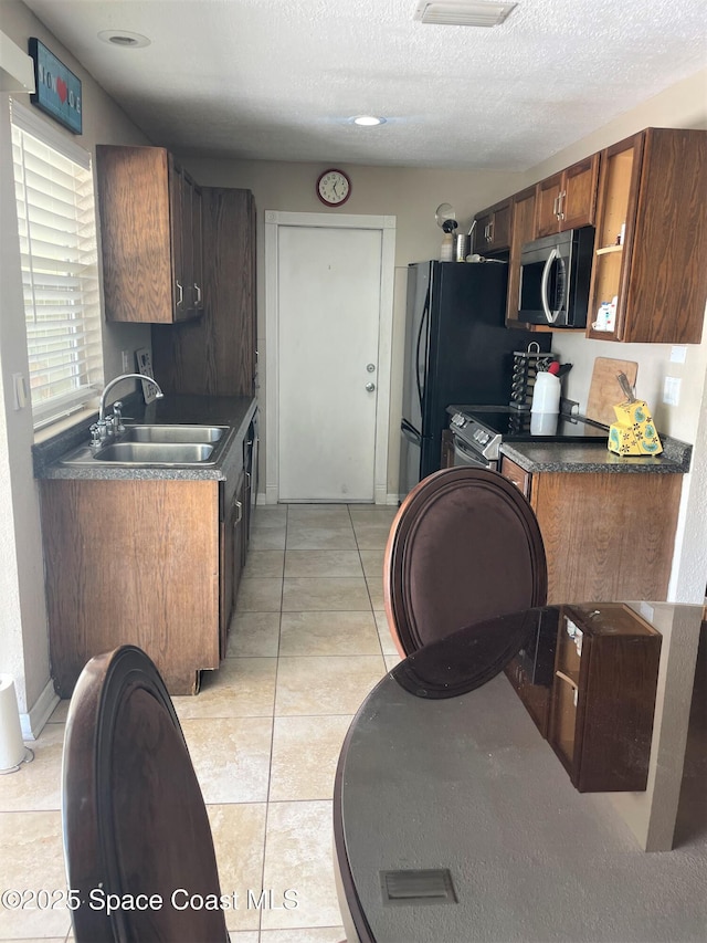 kitchen with dark countertops, a sink, light tile patterned flooring, electric range oven, and stainless steel microwave