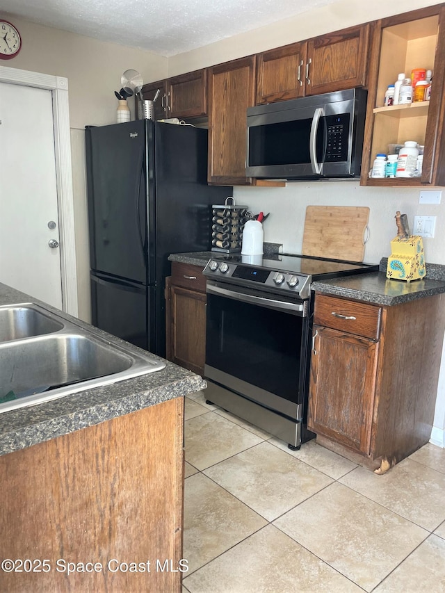 kitchen with dark countertops, light tile patterned floors, stainless steel appliances, and a sink