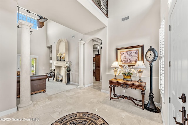 foyer entrance with ornate columns, a towering ceiling, arched walkways, baseboards, and plenty of natural light
