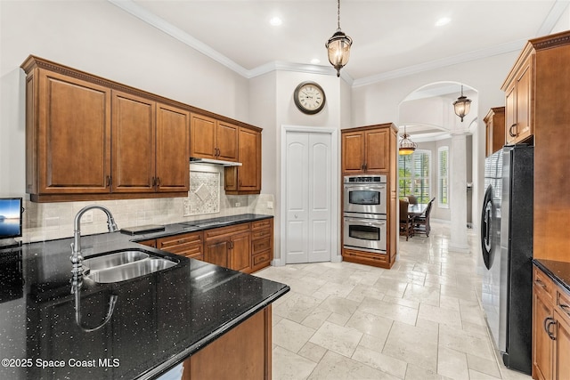 kitchen featuring stainless steel appliances, arched walkways, a sink, ornate columns, and backsplash