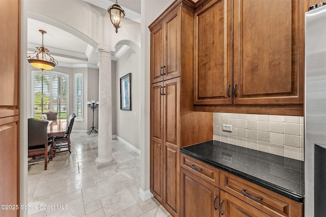 kitchen featuring arched walkways, baseboards, crown molding, ornate columns, and decorative backsplash