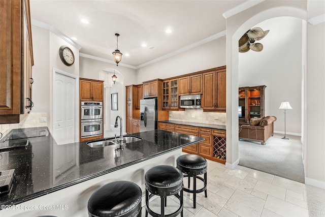 kitchen with appliances with stainless steel finishes, a sink, a peninsula, brown cabinets, and crown molding