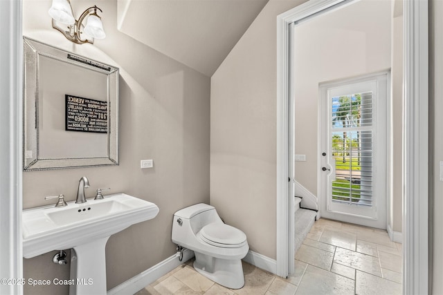 bathroom featuring toilet, baseboards, stone tile floors, and lofted ceiling