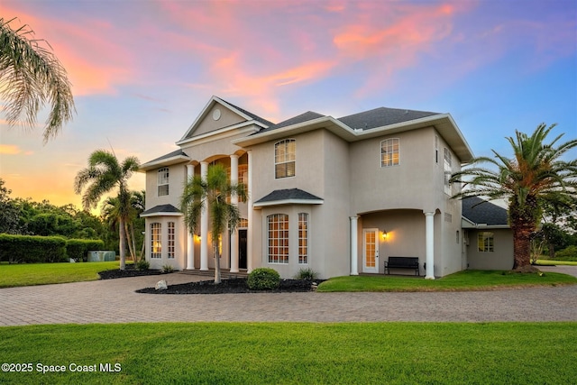 view of front of property featuring a yard, stucco siding, and curved driveway