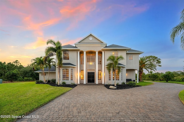 greek revival house with decorative driveway, stucco siding, and a yard