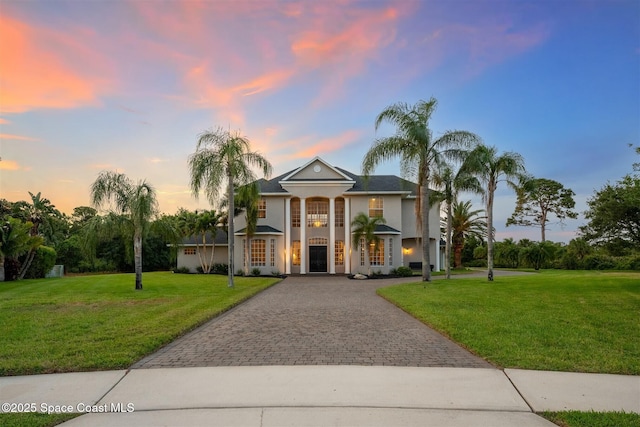greek revival inspired property with decorative driveway, a lawn, and stucco siding