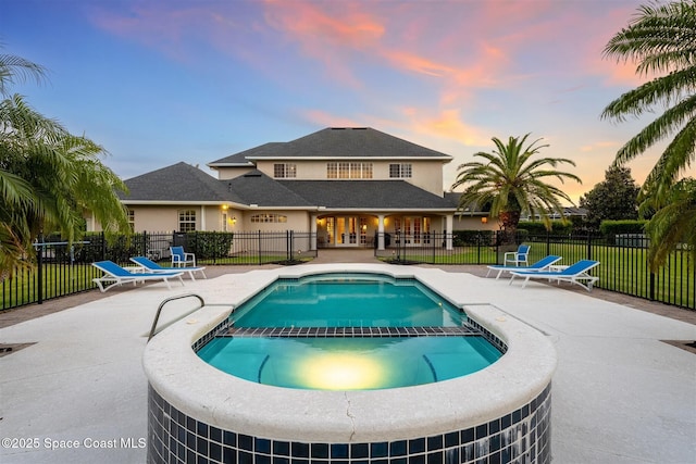 pool at dusk with a patio area, a pool with connected hot tub, and fence