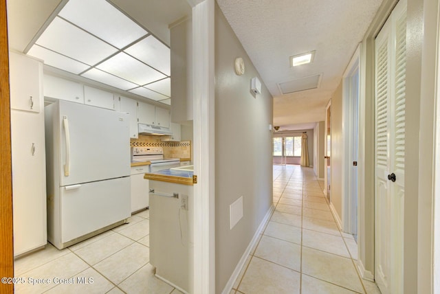 hallway featuring attic access, light tile patterned floors, and baseboards