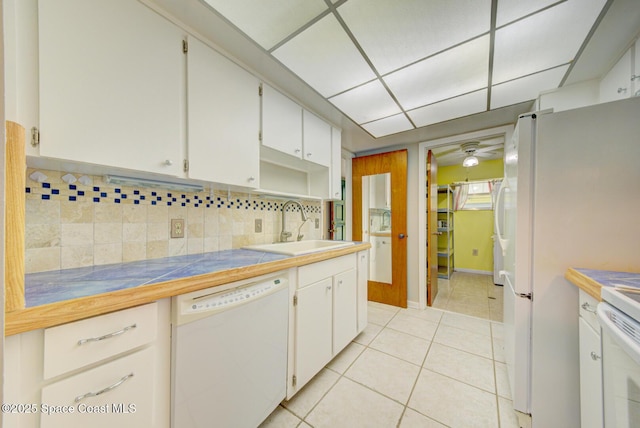 kitchen with white appliances, backsplash, light tile patterned flooring, white cabinets, and a sink