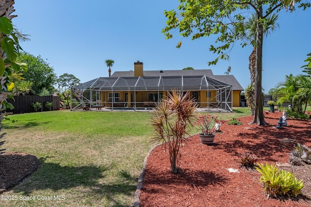 rear view of house featuring a lawn, glass enclosure, fence, and a chimney