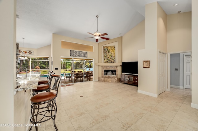 living area featuring tile patterned flooring, baseboards, high vaulted ceiling, a tile fireplace, and a ceiling fan