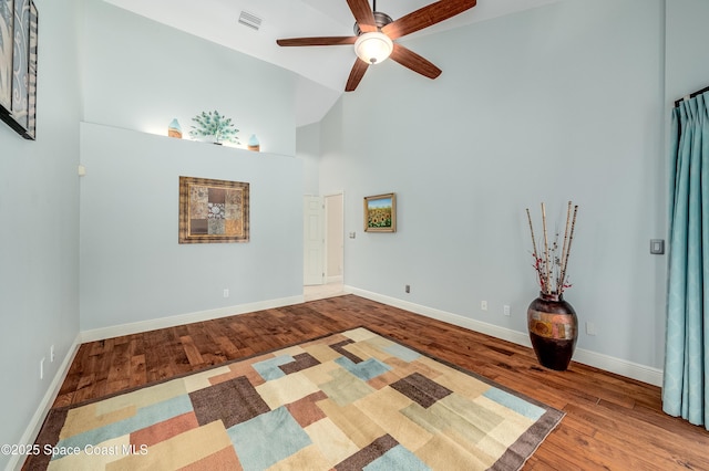 empty room featuring ceiling fan, high vaulted ceiling, baseboards, wood finished floors, and visible vents