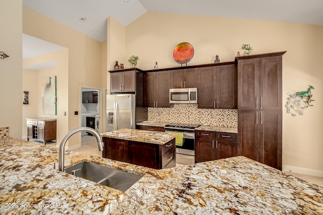 kitchen with decorative backsplash, dark brown cabinets, light stone counters, a sink, and stainless steel appliances