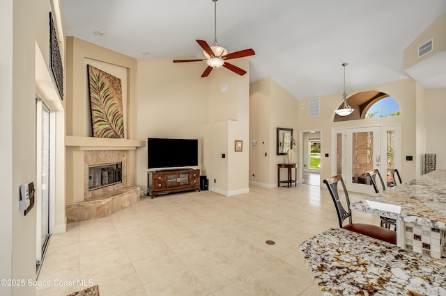 tiled living room featuring visible vents, a ceiling fan, a fireplace, and high vaulted ceiling