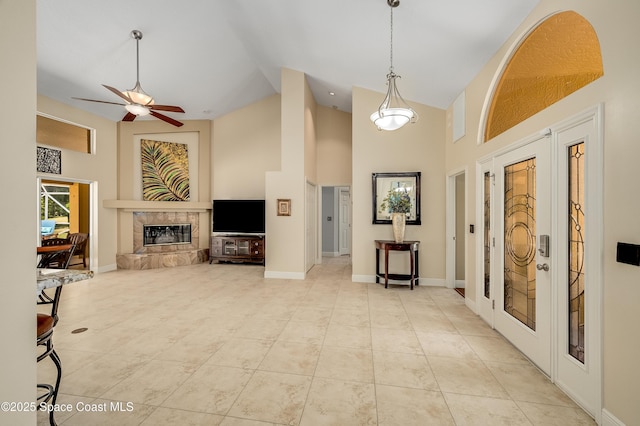 living room featuring a fireplace, high vaulted ceiling, a ceiling fan, baseboards, and light tile patterned floors